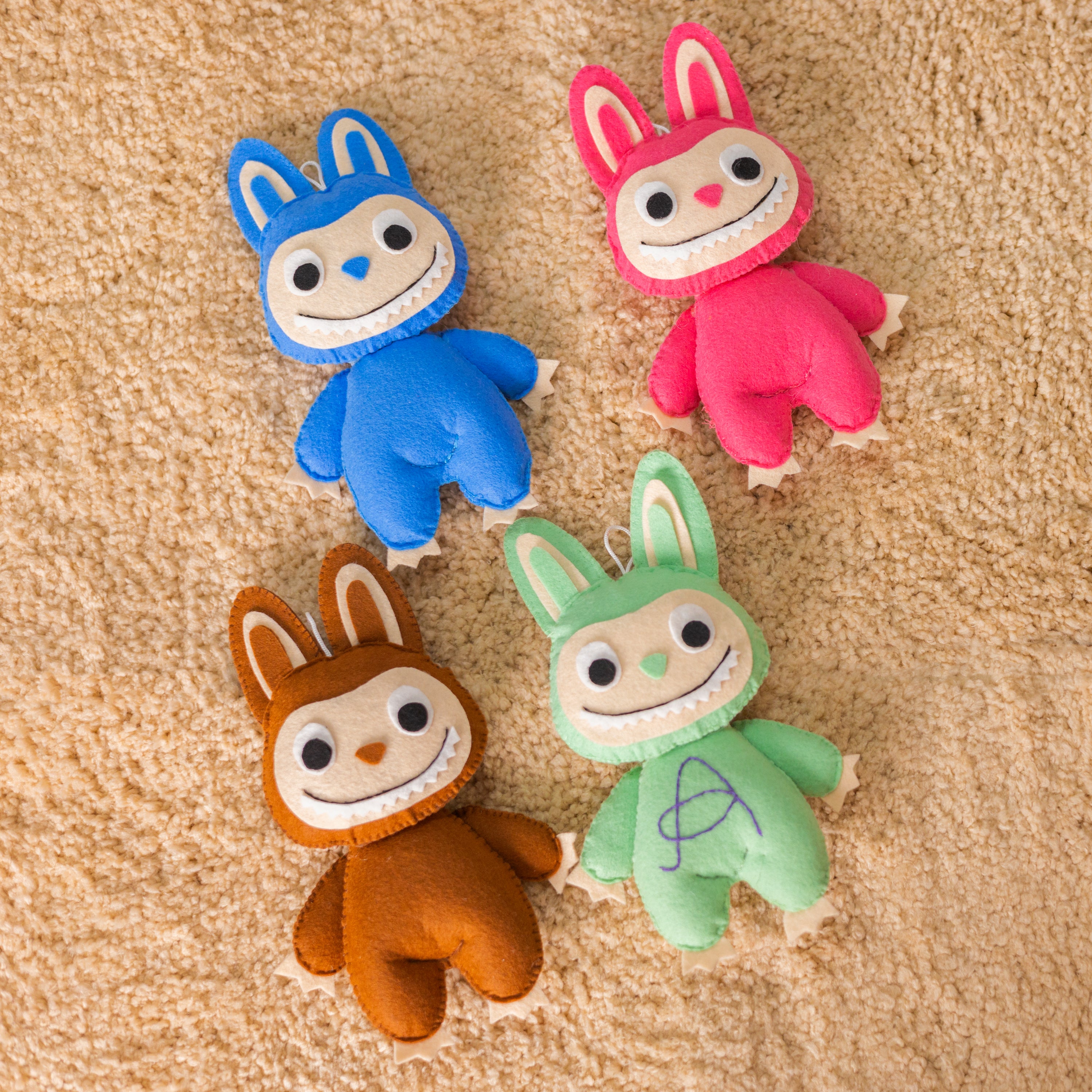 Four colorful plush toys with bunny ears on a beige surface