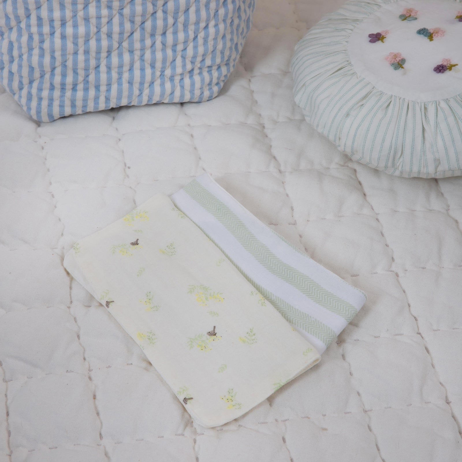 Baby items including a basket with teddy bears, a quilted blanket, and a small pillow on a white surface.