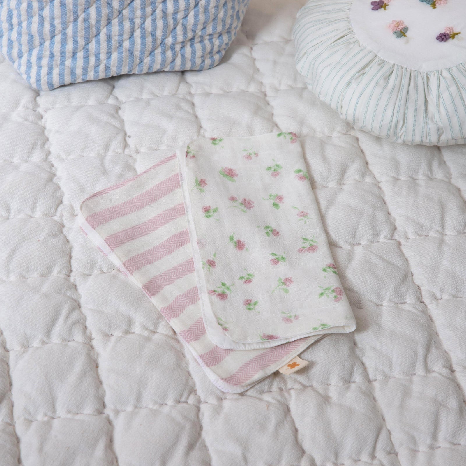 Baby blankets with pink stripes and floral patterns on a white quilted surface.