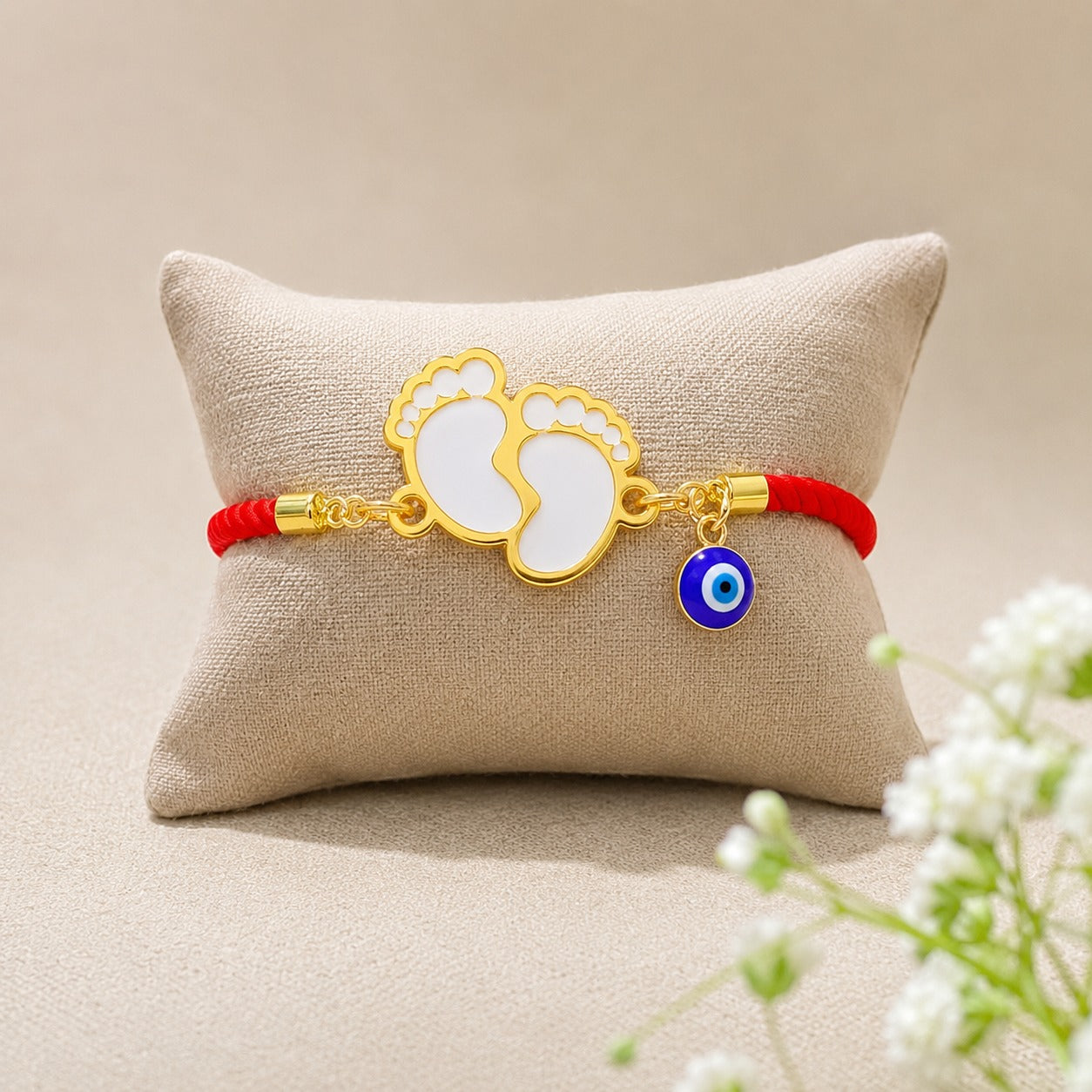 Personalized baby feet acrylic rakhi for newborns with white and gold foot motifs, evil eye charm and red adjustable bracelet.
