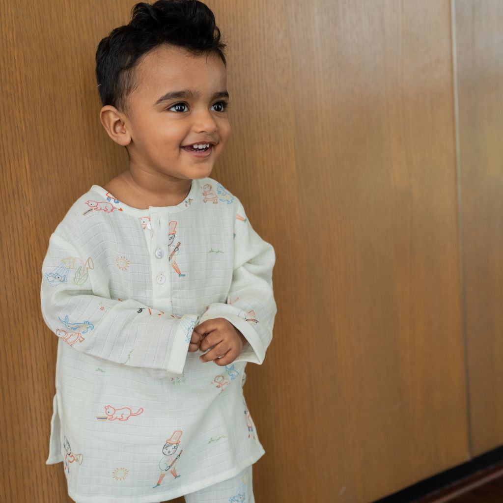 Child wearing a light-colored outfit with patterns standing against a wooden wall.