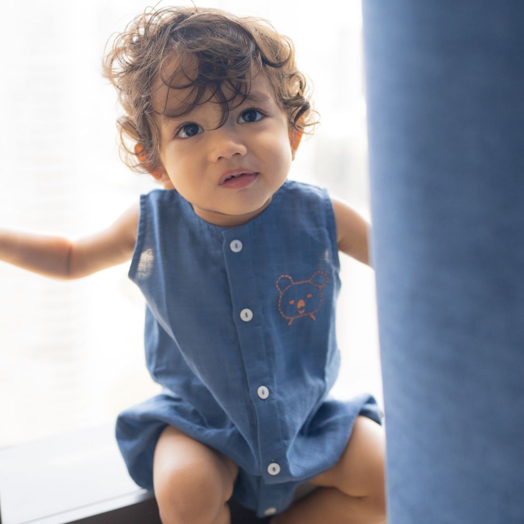 Child wearing a blue sleeveless dress with a bear design, sitting on a white surface.