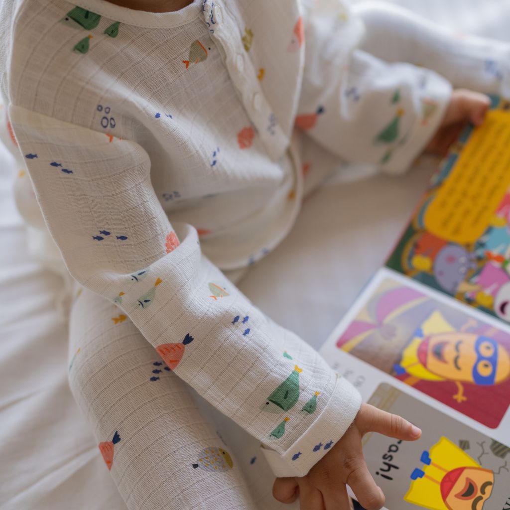 Child wearing a white outfit with colorful patterns, holding a colorful book.