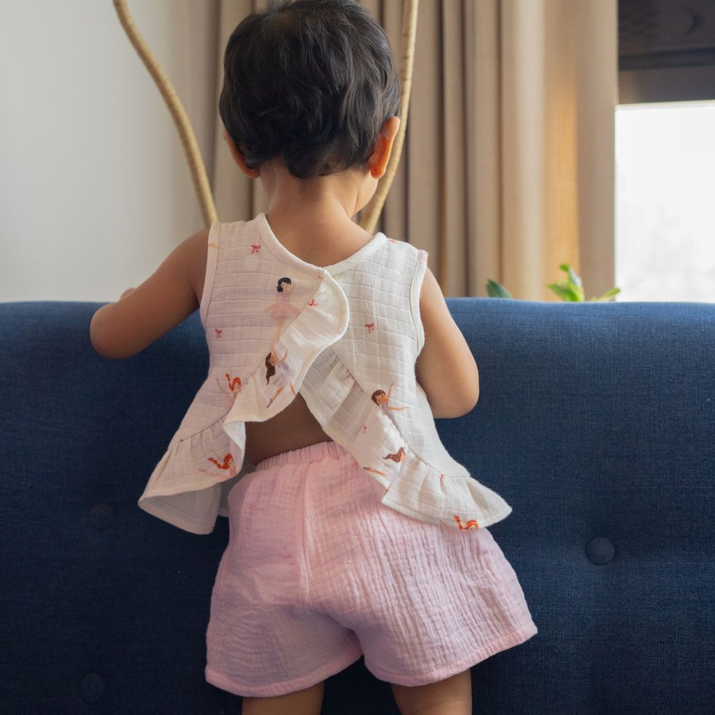 Child wearing a sleeveless top and pink shorts standing on a blue couch.