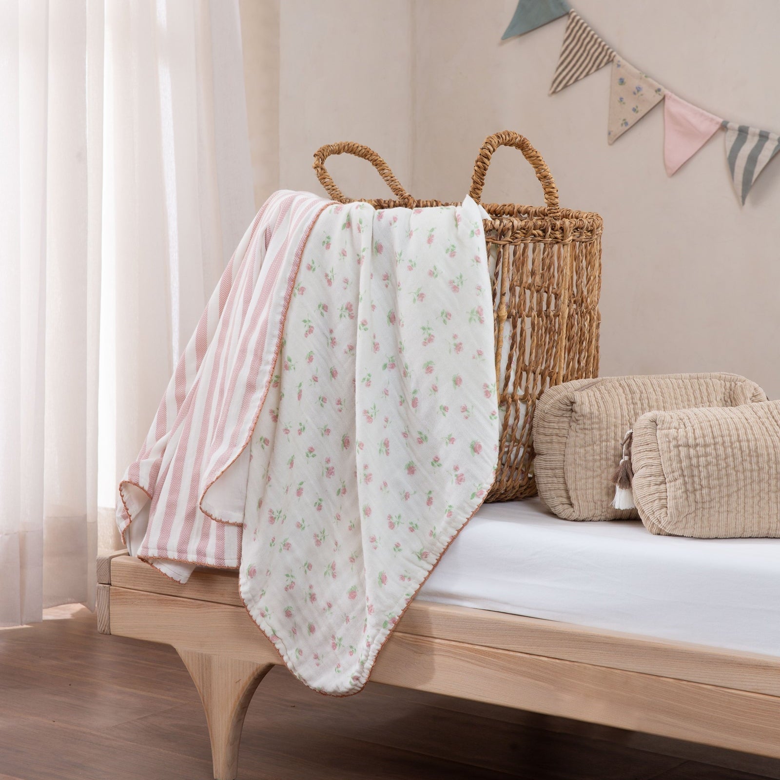 Baby blanket draped over a wooden crib with a wicker basket and decorative flags in the background.