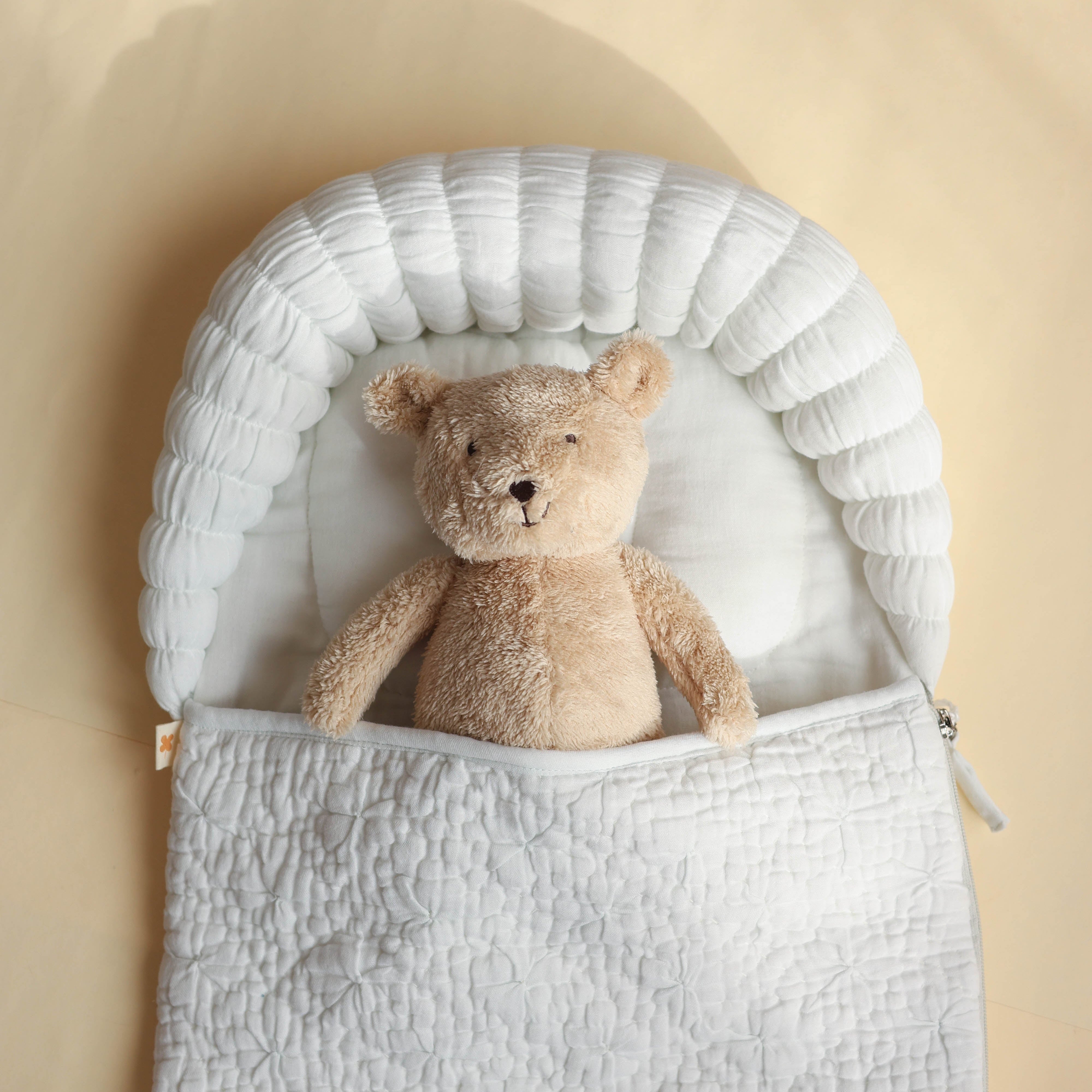Teddy bear inside a white baby bouncer on a beige background