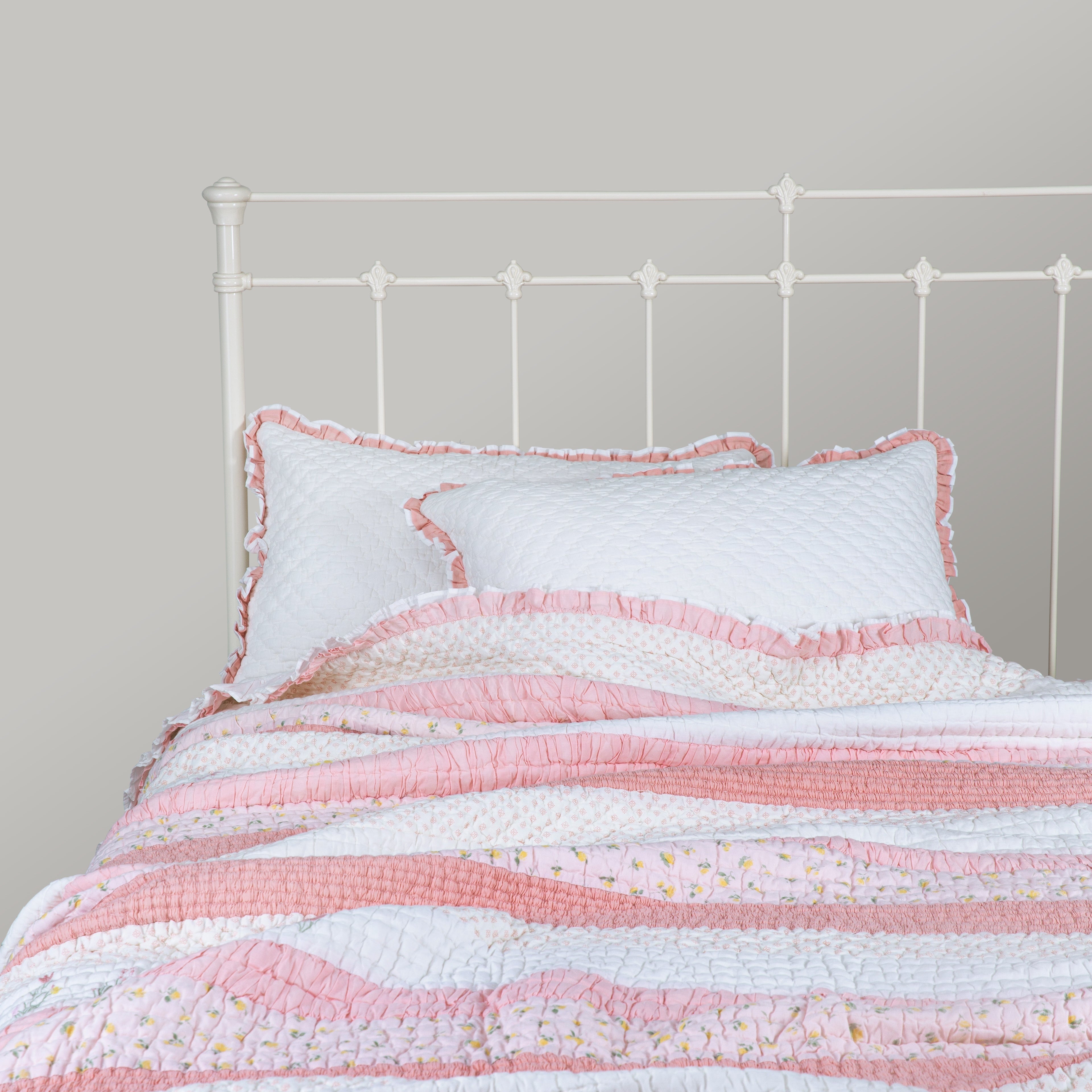 Pink and white striped quilt with matching pillow on a metal bed frame against a gray wall.
