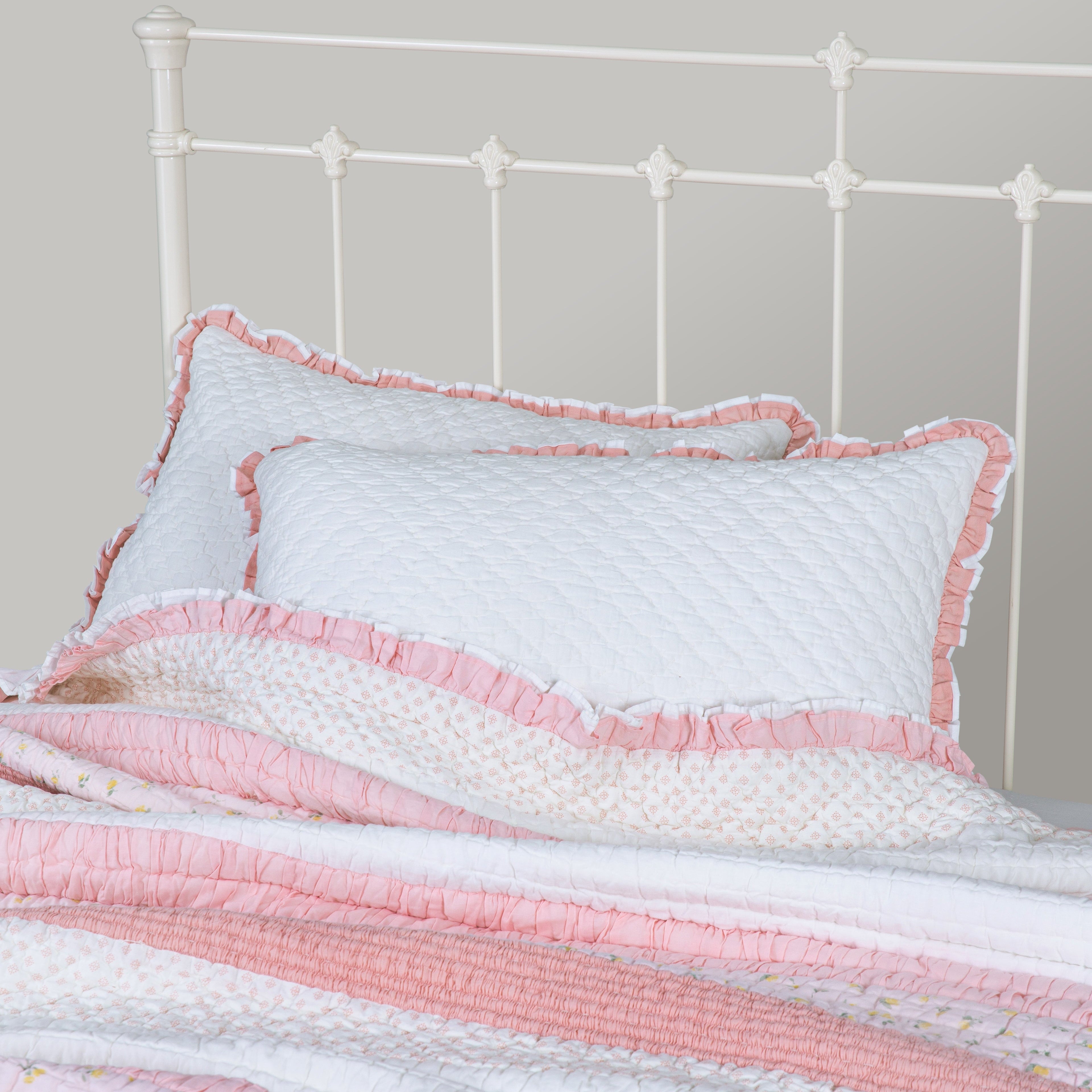 Pink and white striped quilt with matching pillow on a bed against a gray wall.