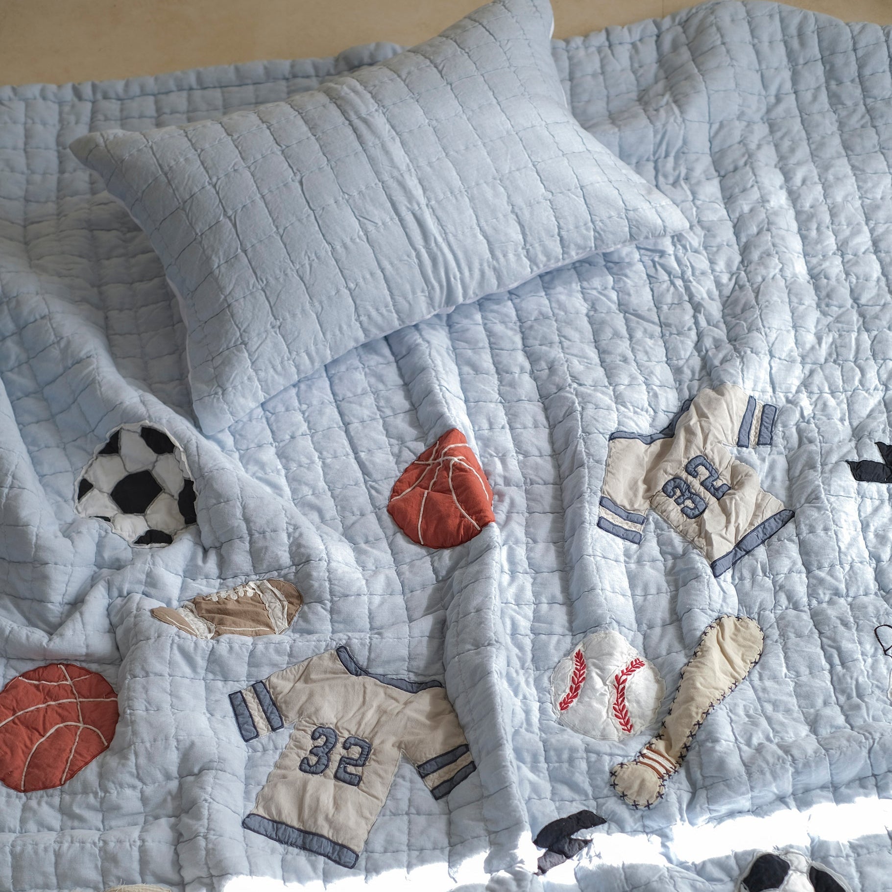 Quilt with sports-themed appliqué including soccer balls, basketballs, and baseball bats on a light blue background.