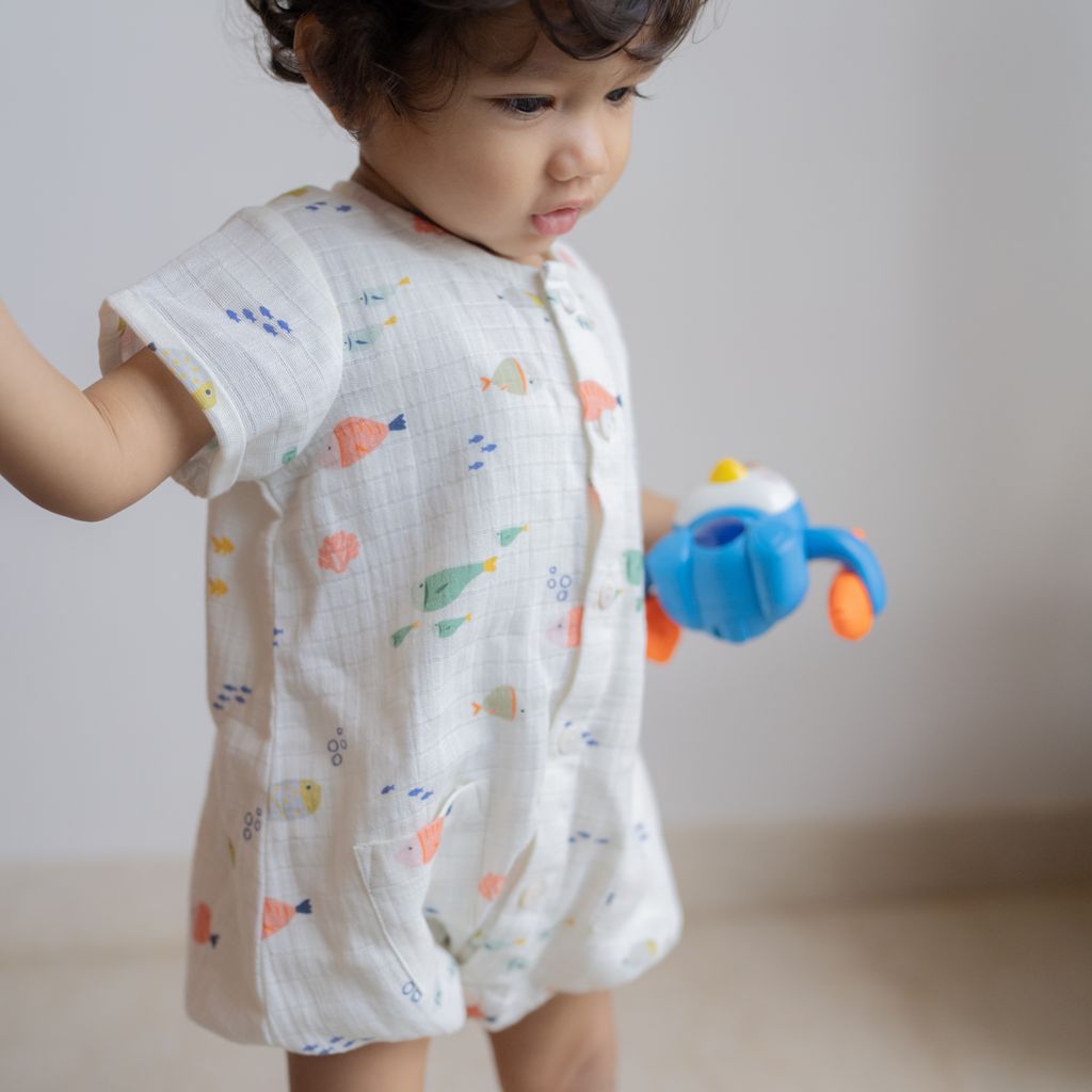 Child wearing a patterned onesie holding a toy with a neutral background