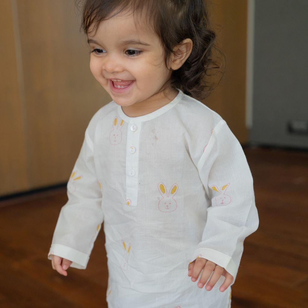 Child wearing a white long-sleeve shirt with bunny designs on a wooden floor.