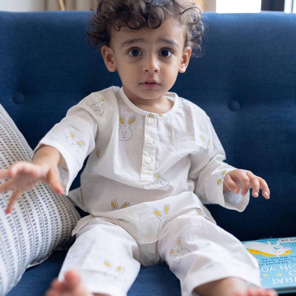 Child sitting on a blue couch wearing a white outfit with yellow patterns.