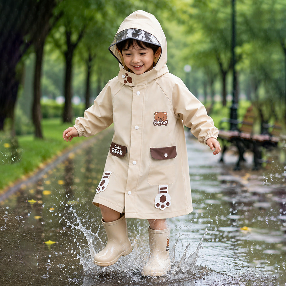 Child in a beige raincoat with bear designs jumping in a puddle in a park.