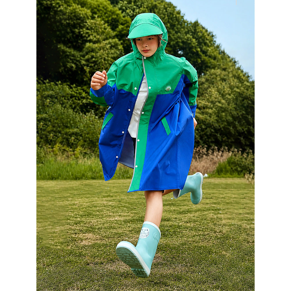 Child wearing a green and blue raincoat running outdoors on grass with trees in the background