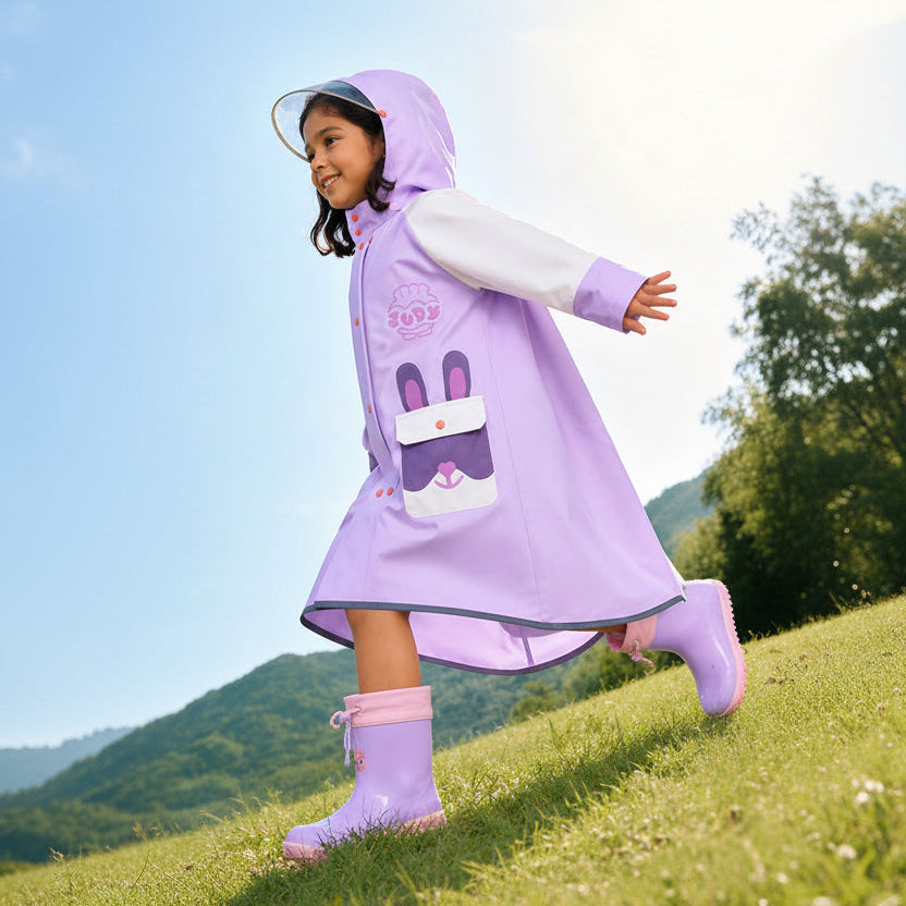 Child wearing a purple raincoat and boots outdoors with mountains in the background