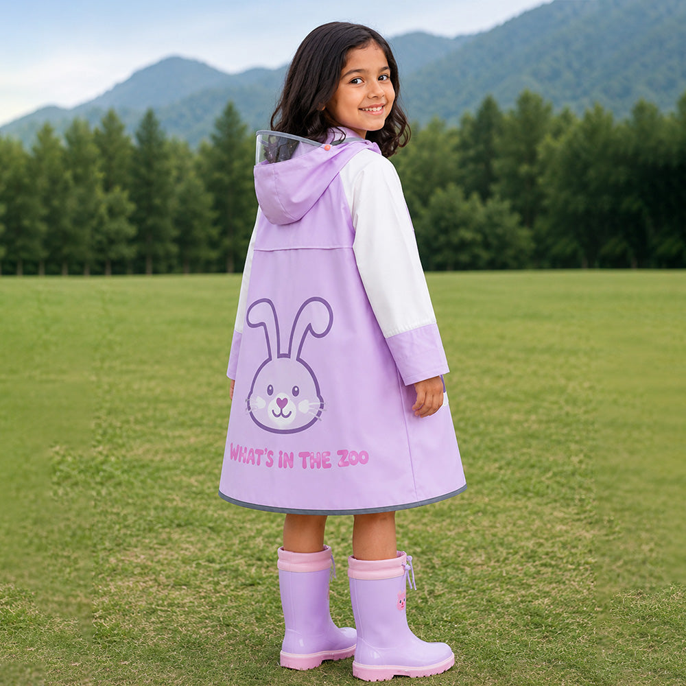 Child wearing a purple raincoat with a bunny design and matching boots in a grassy field with mountains in the background.