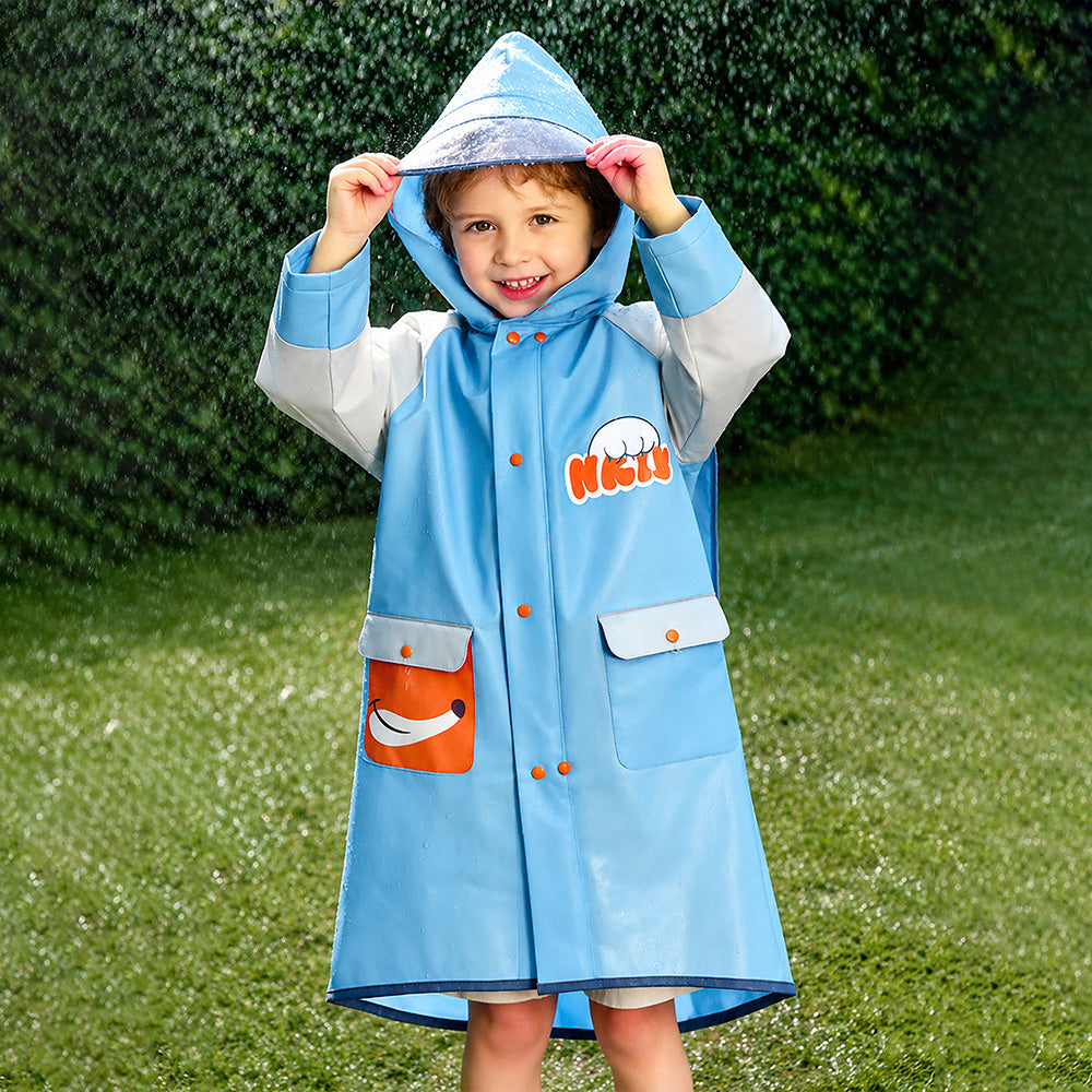 Child wearing a blue raincoat with a hood, standing on grass with greenery in the background