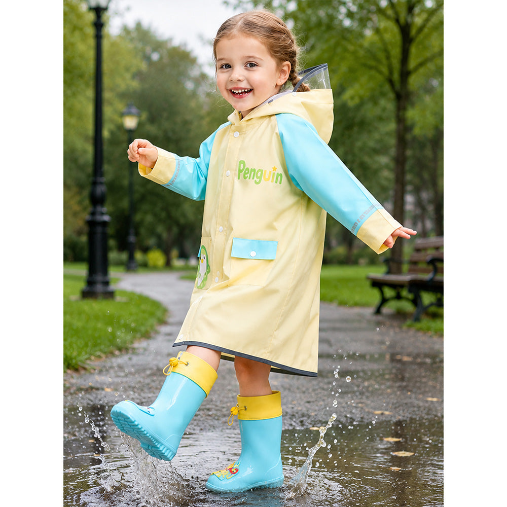 Child wearing a yellow raincoat with a penguin design and blue rain boots, splashing in water.