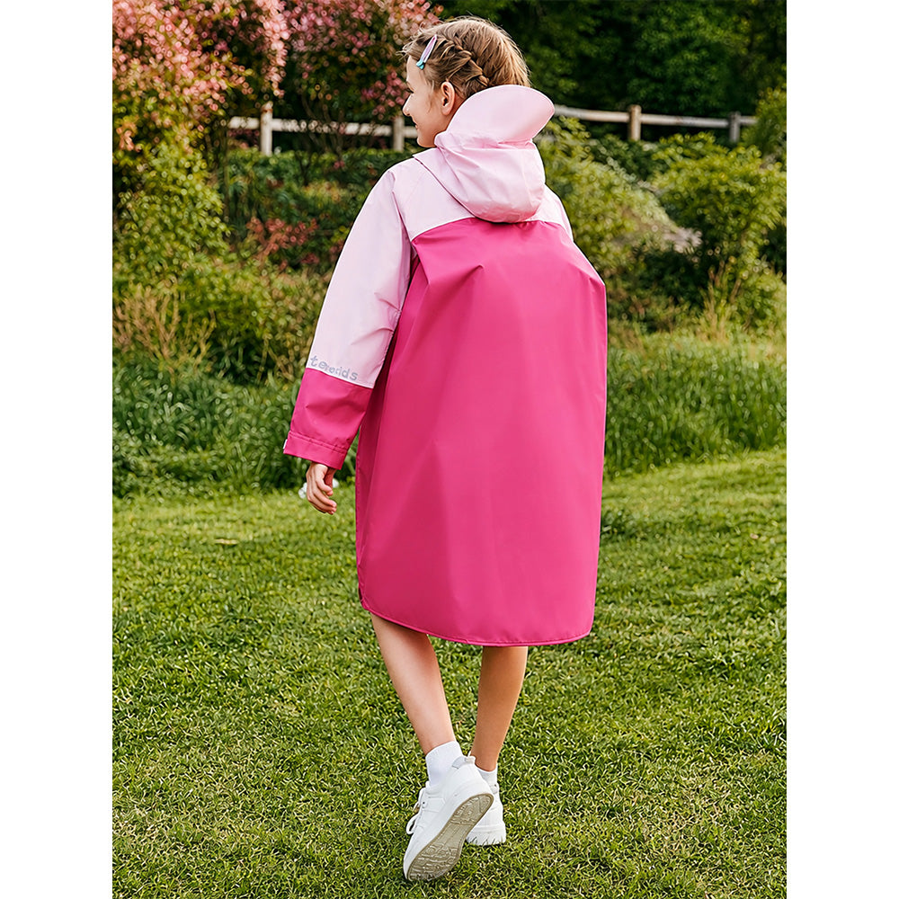 Person wearing a pink and white raincoat standing in a grassy area with trees in the background