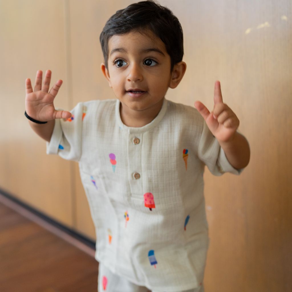 Child wearing a white shirt with colorful ice cream patterns, standing indoors.