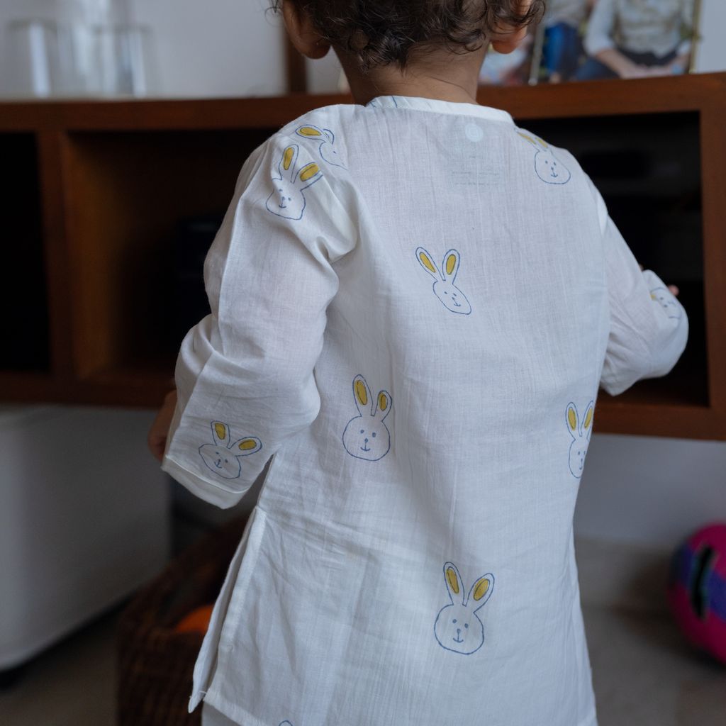 Child wearing a white dress with bunny patterns in a room.