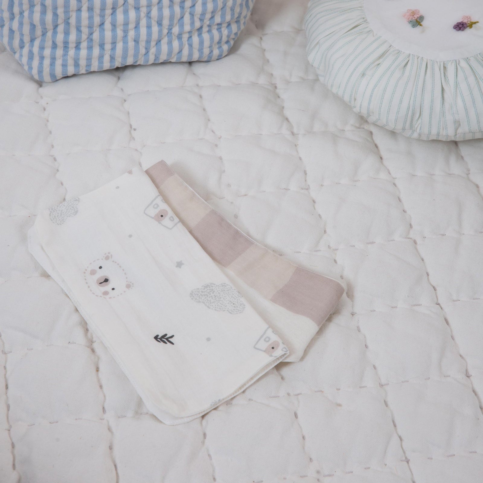 Baby items including a basket with plush toys, a quilt, and a small bag on a textured surface.