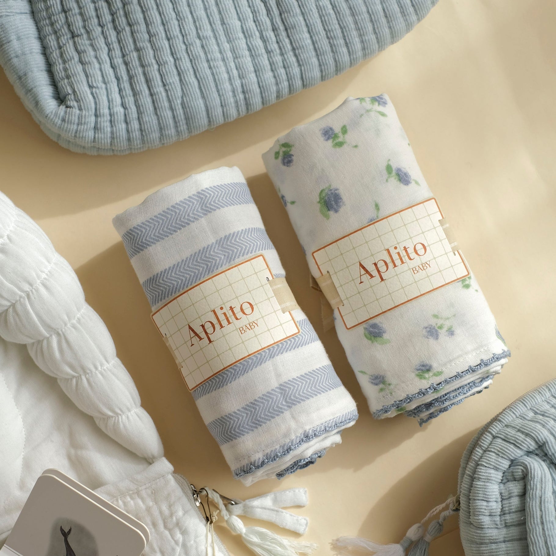 Two folded baby blankets with 'Aplito' branding on a beige surface.