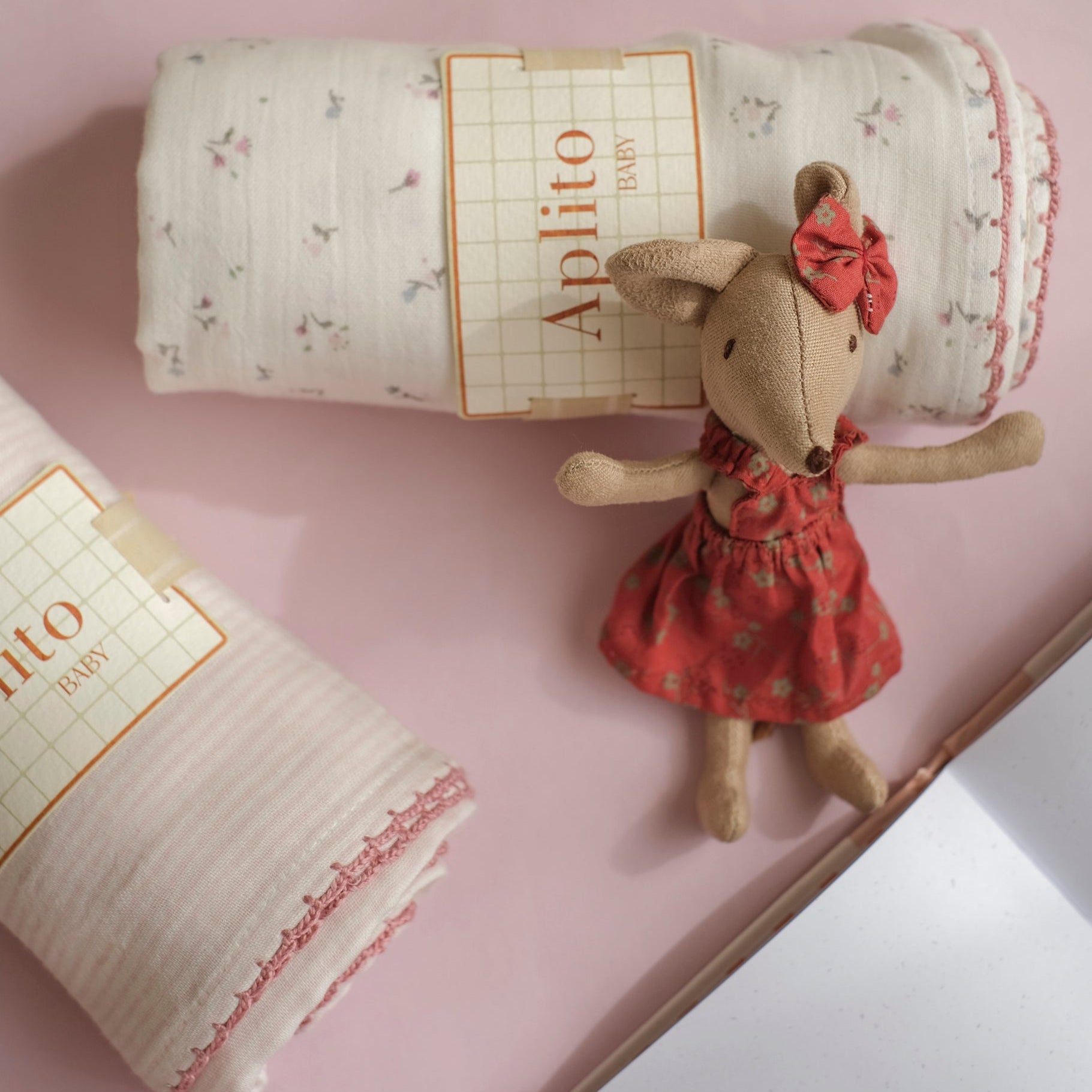 Small plush toy mouse in a red dress next to a roll of paper with 'Aplilo' branding on a pink surface.