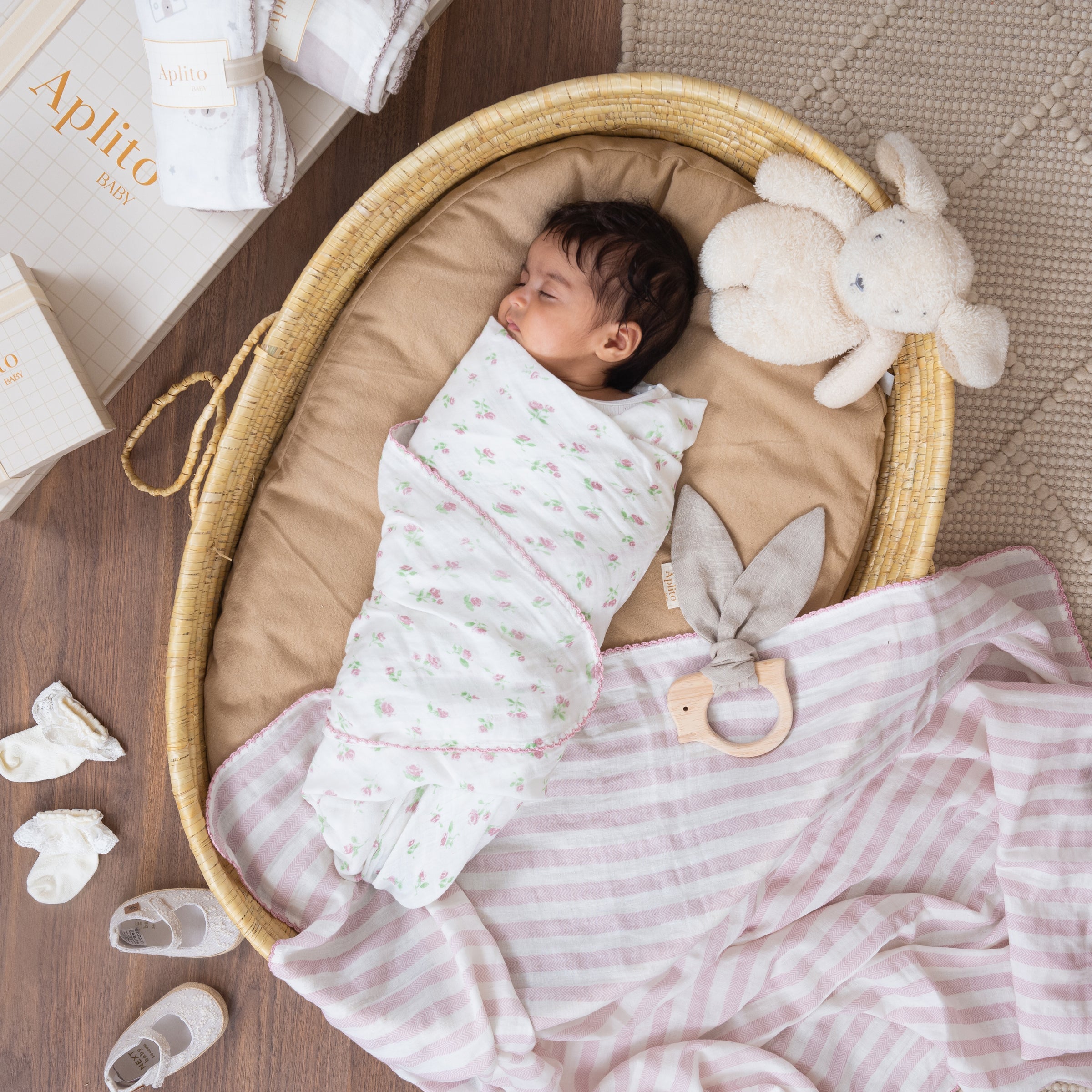 Newborn baby swaddled in a basket with toys and blankets, featuring the brand 'Aplito'.