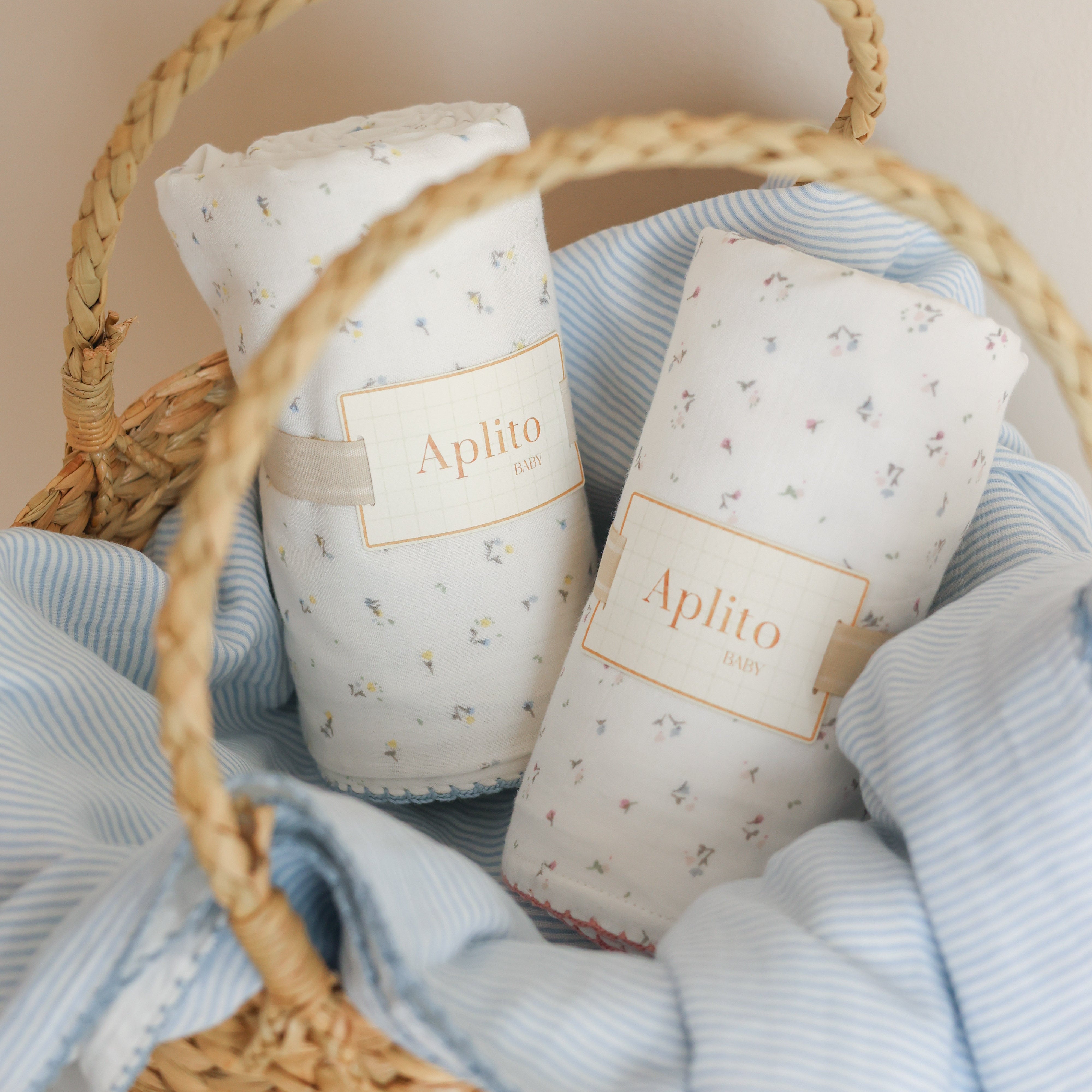 Two baby swaddles with 'Aphito' branding in a woven basket with blue fabric.