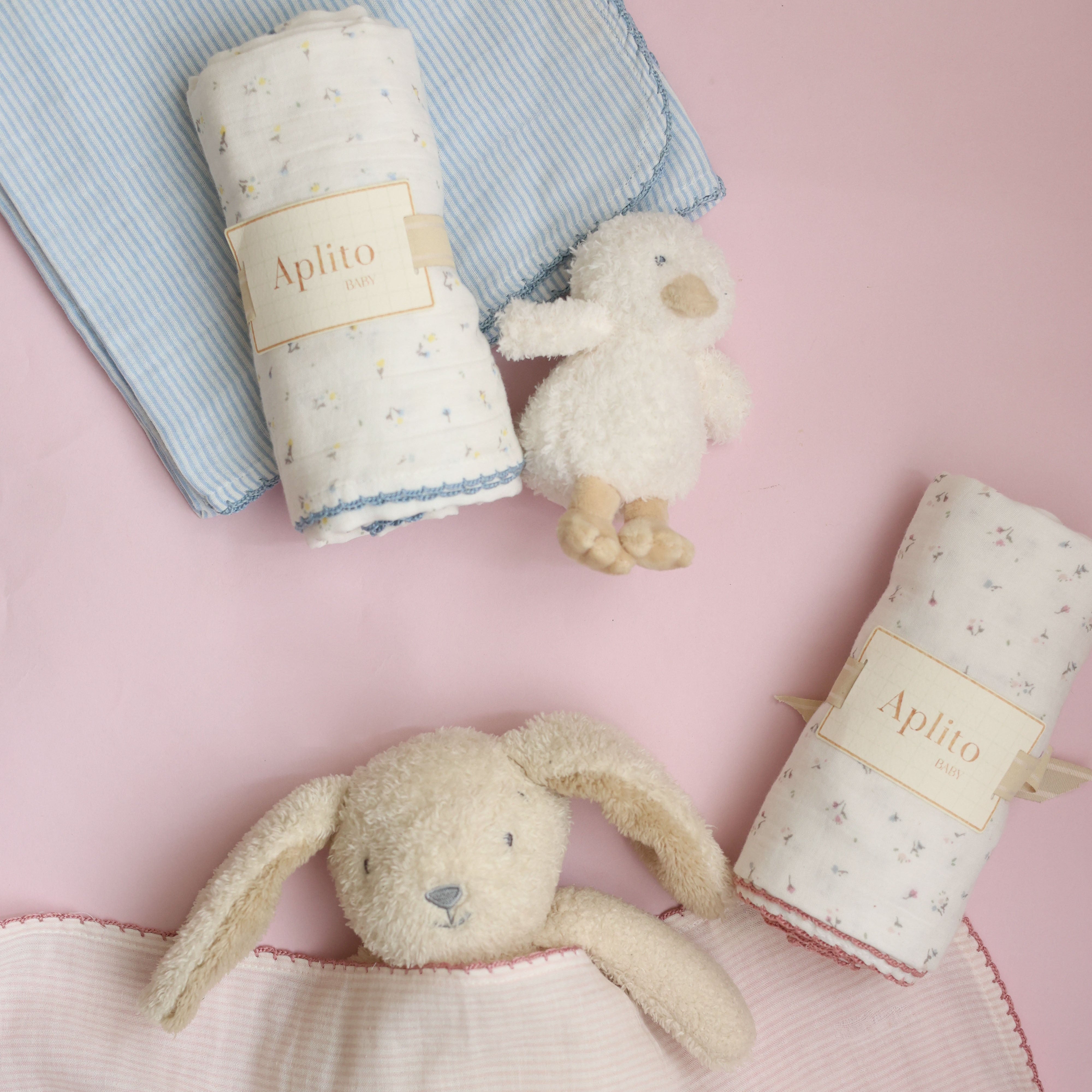 Two plush toys and two rolled-up blankets with 'Aphelo' branding on a pink background.