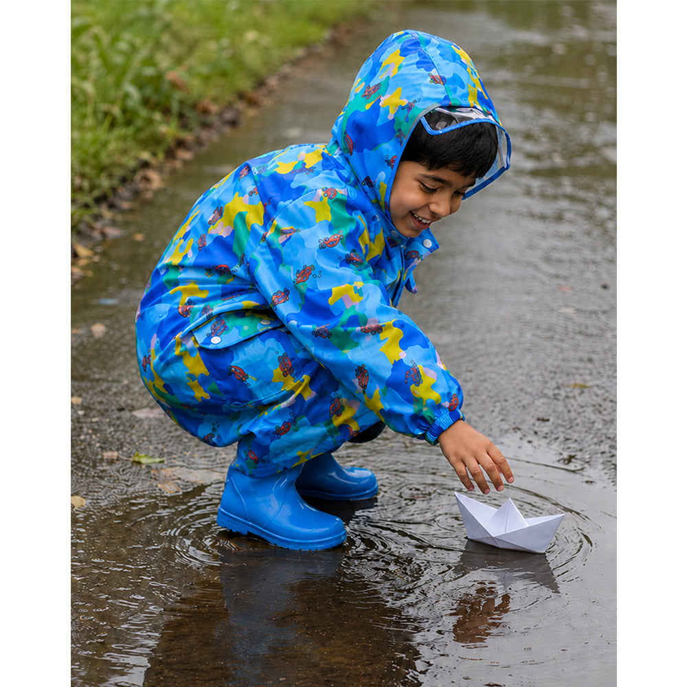 Child playing with a paper boat outdoors in blue color pop kids raincoat and blue rain boots