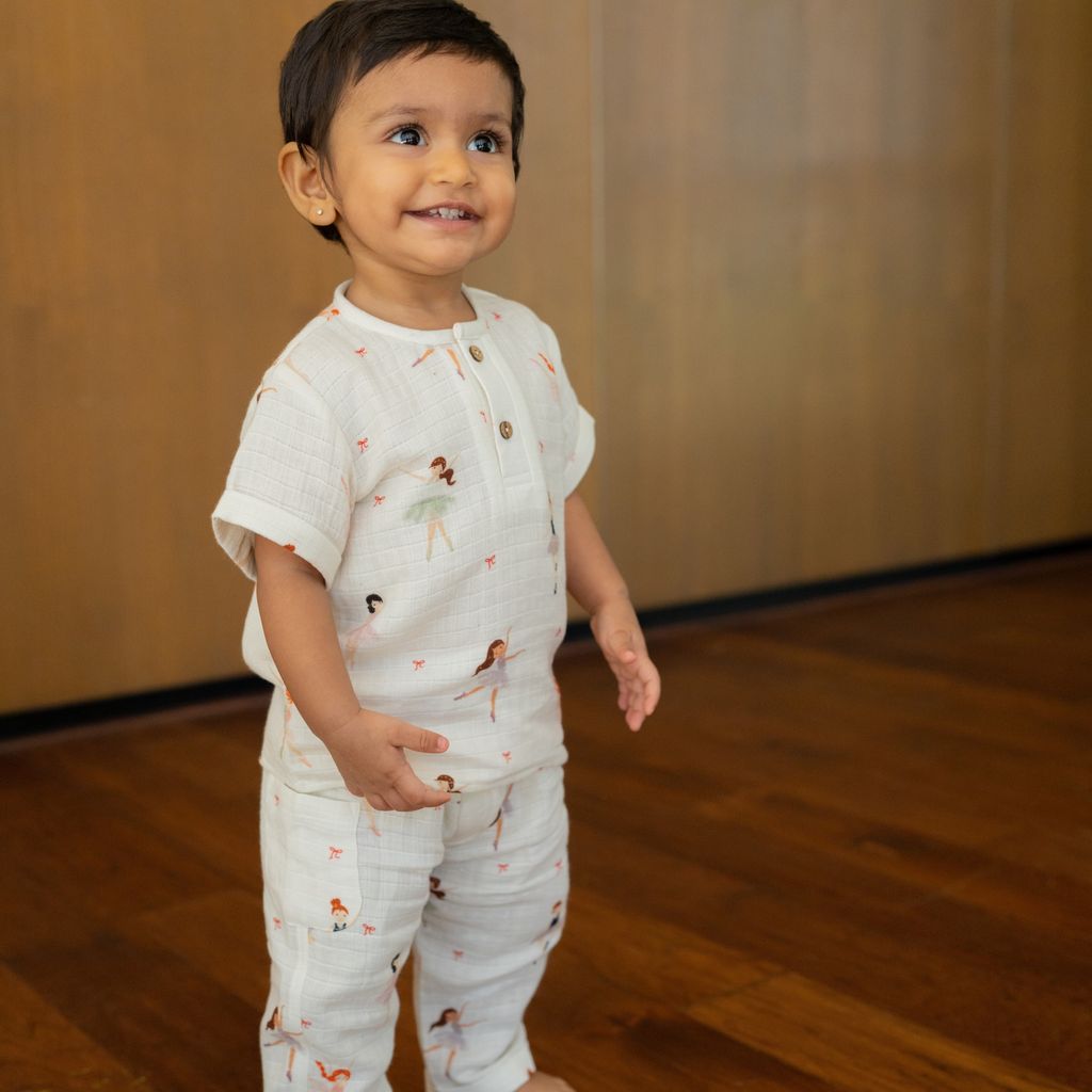 Child wearing a white outfit with animal prints on a wooden floor.