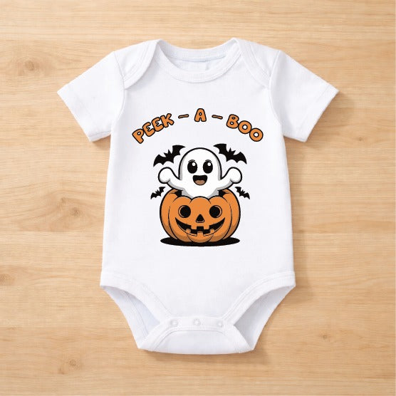 A white short-sleeve baby bodysuit laid flat on a light wood background, featuring a Halloween graphic with the text 'PEEK-A-BOO' above a cartoon ghost popping out of a jack-o'-lantern.
