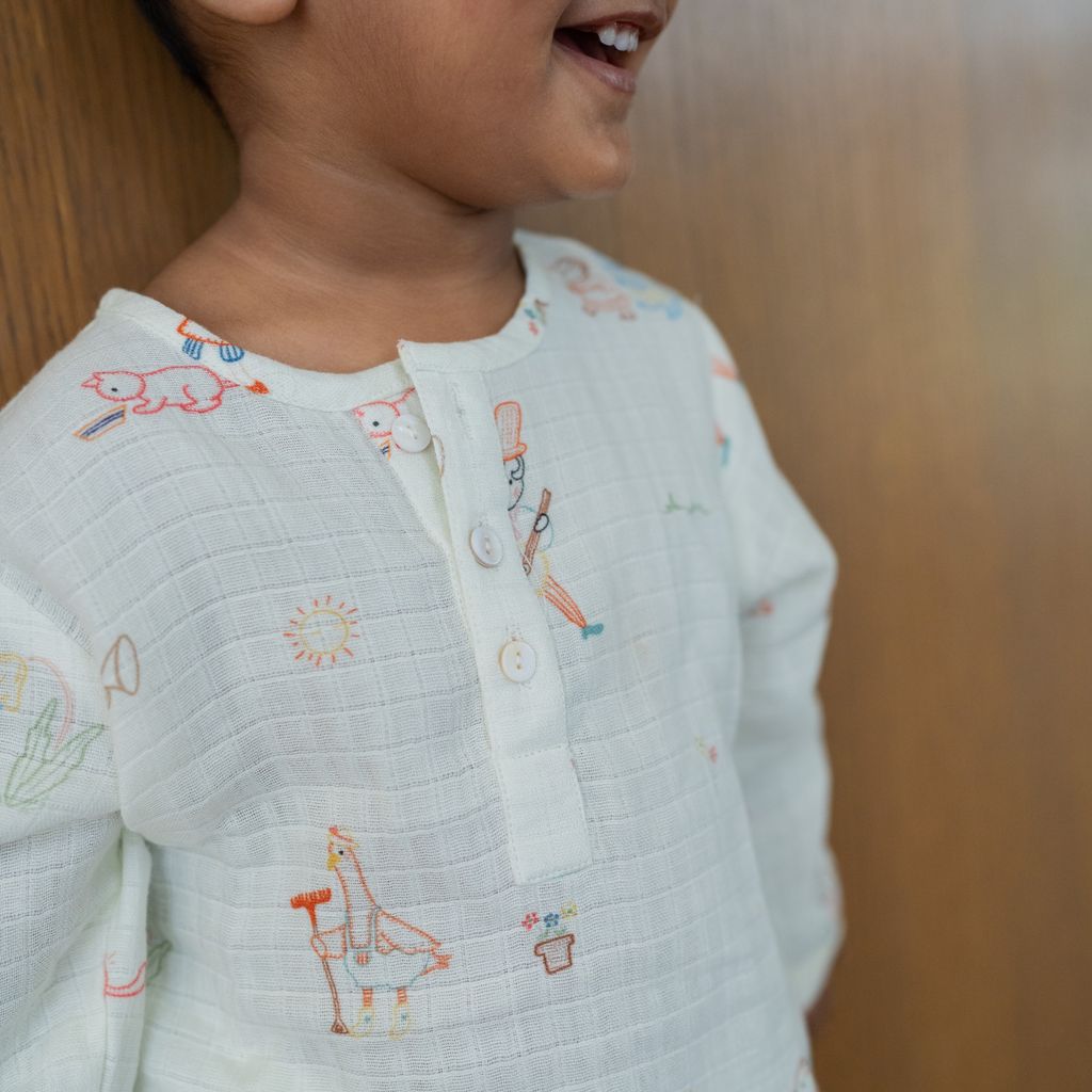 Child wearing a light-colored outfit with embroidered designs on a wooden background