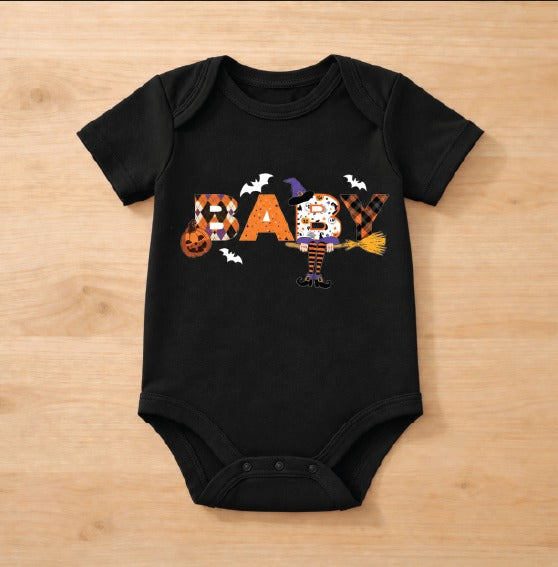 A black short-sleeve baby bodysuit laid flat on a light wood background, featuring a colorful Halloween-themed 'BABY' graphic with a witch character and bats.