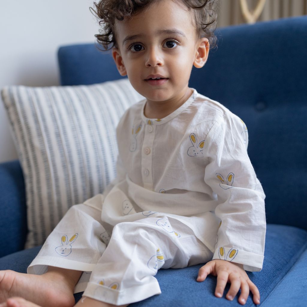 Child wearing a white outfit with bunny designs sitting on a blue couch.
