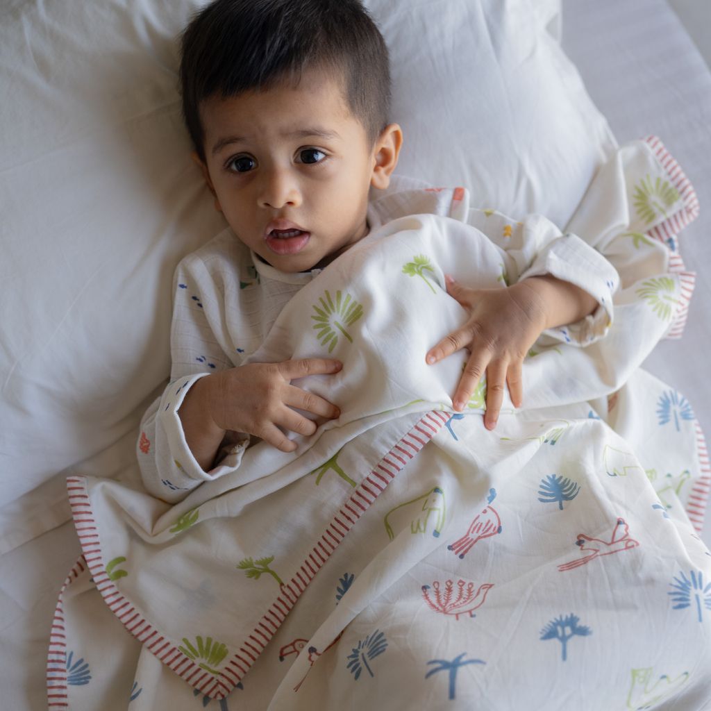 Child wrapped in a patterned blanket on a white bed