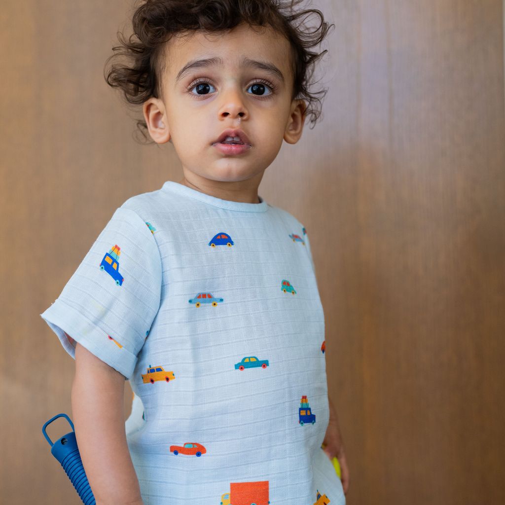 Child wearing a light blue shirt with colorful car patterns against a wooden background