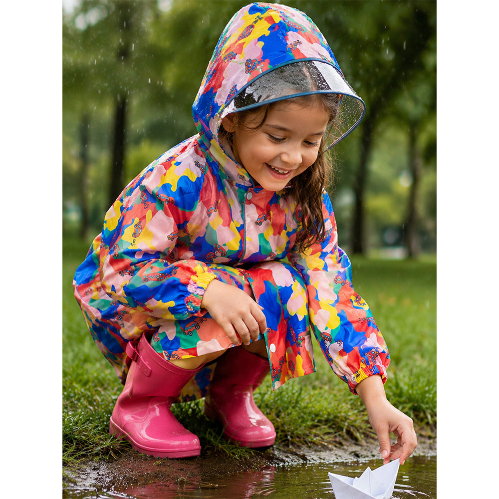 Child crouching outdoors in pink color pop kids raincoat and pink rain boots during rain