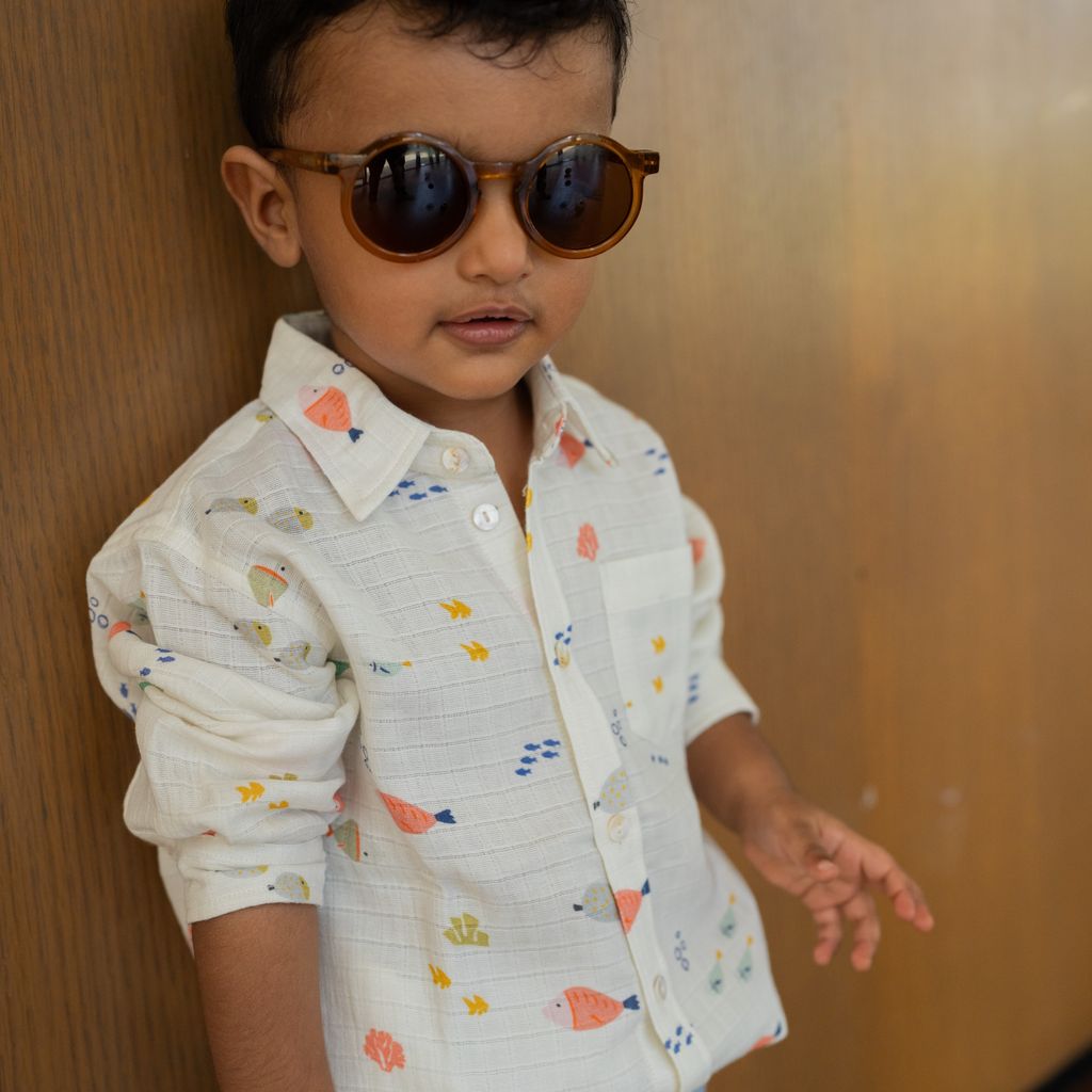 Child wearing a patterned shirt and sunglasses against a wooden background