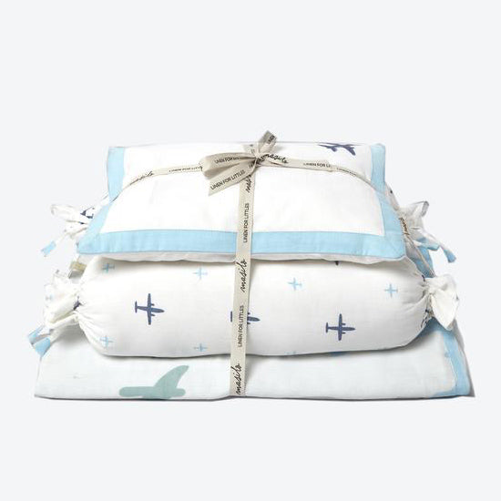 A set of baby cot bedding with a sky blue and white theme, including a pillow and blankets with airplane and star patterns, tied together with a string.